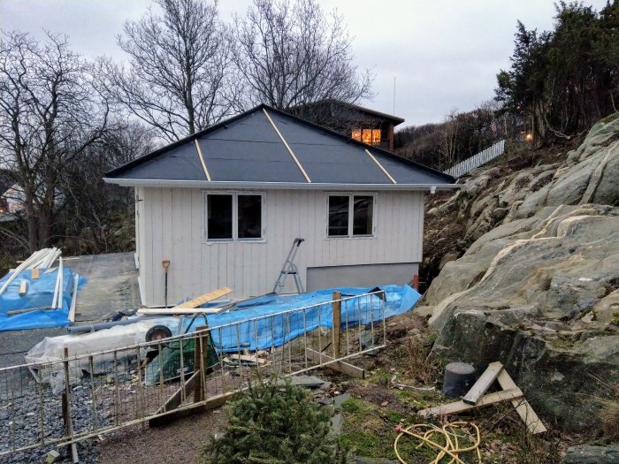 Nyinstallerade fönster på ett hus under renovering med byggmaterial synligt och naturlig bergig bakgrund.