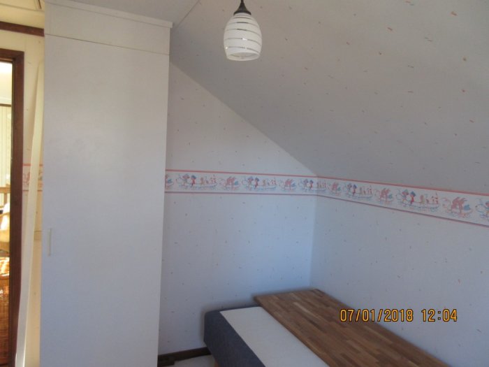 Tidigare barnrum redo för renovering med gammalt skrivbord, tapet med bård och snedtak.