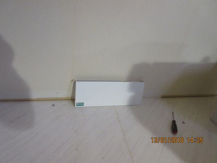 Nedmonterat golv-tilluftsdon vid hörn på knarrigt golv med skruvmejsel, redo för renovering.