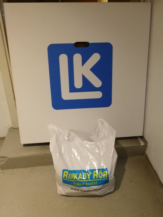 Plastpåse från Rinkaby Rör framför en vit kartong med LK-logotyp, insinuerar köp av VVS-produkter.