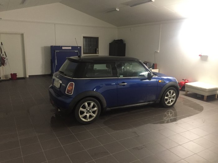 Blå MINI Cooper parkerad i rymligt garage med grått golv och vita väggar.