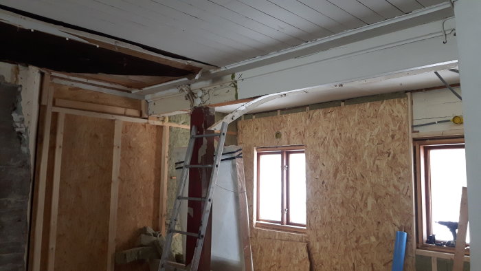 Renoveringsprojekt med exponerade takbjälkar och OSB-skivor på väggen, med stege och fönster.
