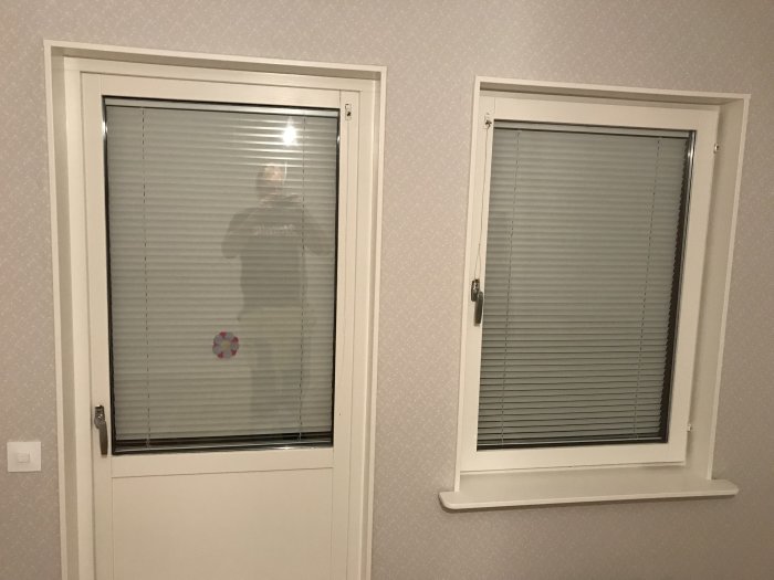 Två fönster med nyinstallerade persienner i ett rum med tapetserade väggar.