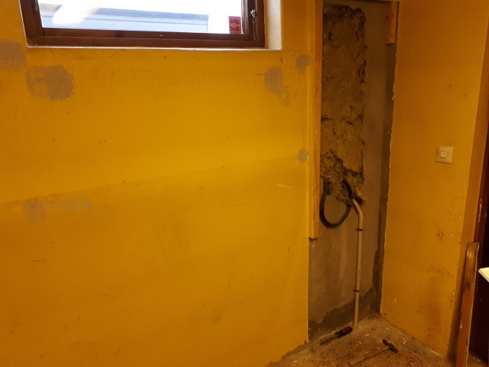 Renoveringsprojekt i ett garage med partiellt avsliten gipsskiva och spacklade hål på en gul vägg.