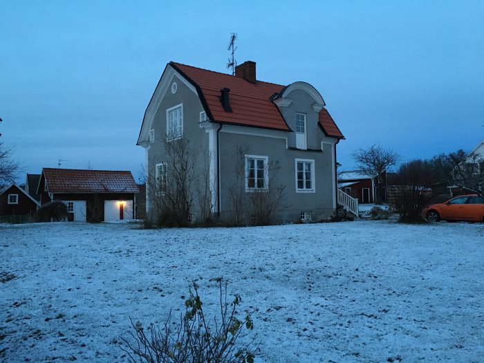 Ett hus i skymningen med snö på marken, fönstret i mitten på entreplan och en svart ventilationskåpa ovanför.