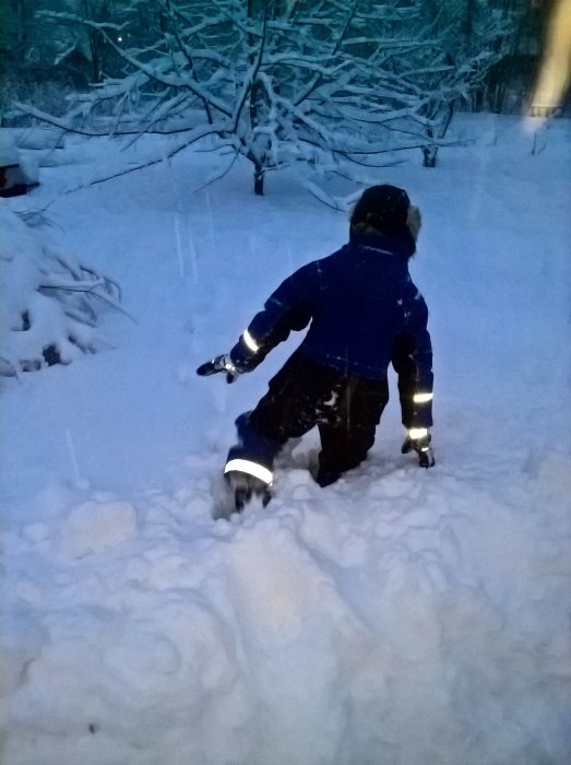 Barn som leker i djup snö på en trädgård under kraftigt snöfall.