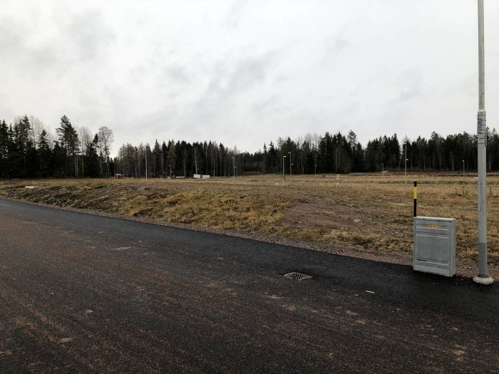 Tomt med pågående markarbete vid skogskant, schaktat område synligt med gräs och jord.