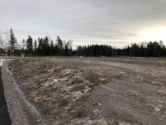 Tomt med lätt snötäcke före schaktning, utsättningspinnar synliga, ingen grävmaskin närvarande.