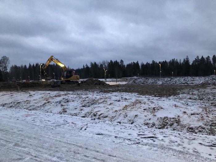 Grävmaskin som utför schaktningsarbete på en tomt med synliga högar av matjord och utjämning av marken.