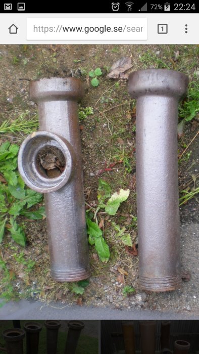 Två gamla gjutjärnsavloppsrör stående i gräs mark, möjligen från en källare.