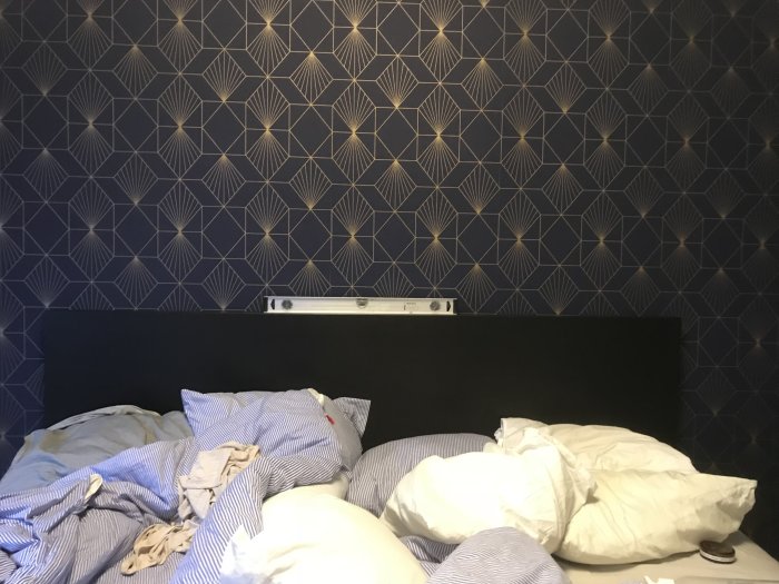 Vattenpass ovanpå en sänggavel mot en tapetserad vägg med geometriskt mönster, visar vågrät nivå.