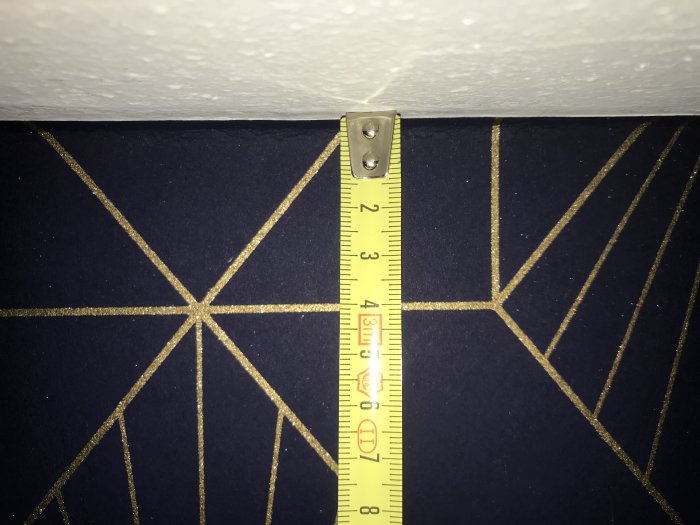 Måttband visar sned tapet med geometriskt mönster vid taket, mindre än 2 cm skillnad över 4,2 m.