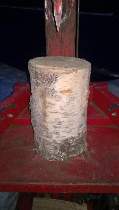 Björkvedskubbe på 30 cm tjocklek redo att klyvas, ligger på röd vedklyv.