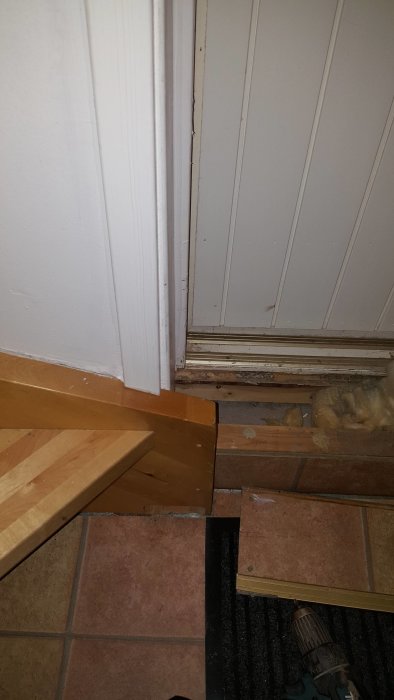 Golvtröskel vid dörröppning med synliga reglar och en del av en trappstegskant, med borr i förgrunden.