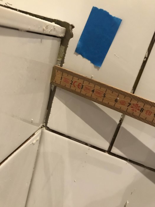 Ojämnt skuren kakelplatta i hörn med varierande fogbredder mätta med tumstock.