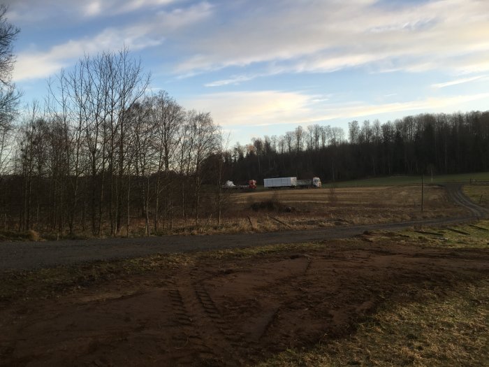 Grävplats med uppkörda stenar i hög, grusväg med lastbil i bakgrunden och spår efter arbete i marken.