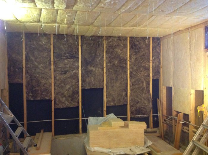 Isolerat garage under renovering med upplyft takisolering, träreglar och material på golvet.