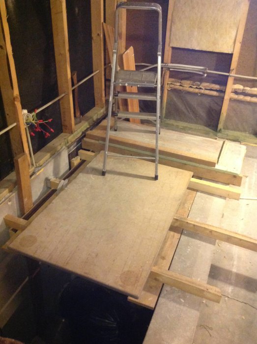 En stege på en hemgjord träplattform över en trappa i ett renoveringsprojekt inne i en byggnad.