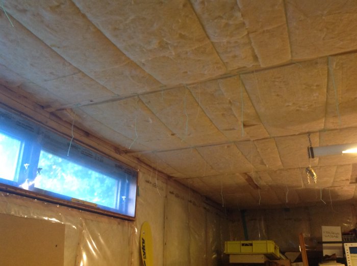 Isolerat garage med synlig takisolering och plastfolie, små glasfönster och mög på pallar.