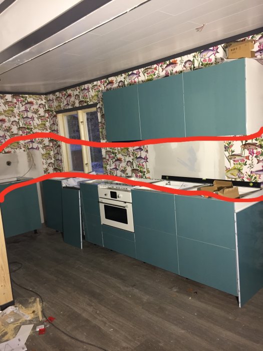 Kök under renovering med blå skåp och bänkskiva, vägg med blommigt tapet och markerad kakelyta.