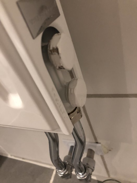 Radiator med övre mutter som läcker vatten, rostfläckar synliga, omgivet av kakelvägg.