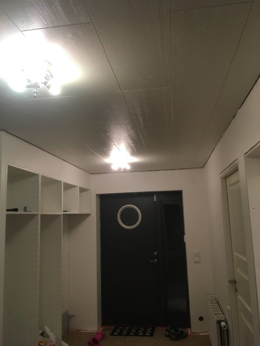 Nyinstallerat tak i trästruktur med infällda spotlights i ett rum med vit vägg och svart ytterdörr.