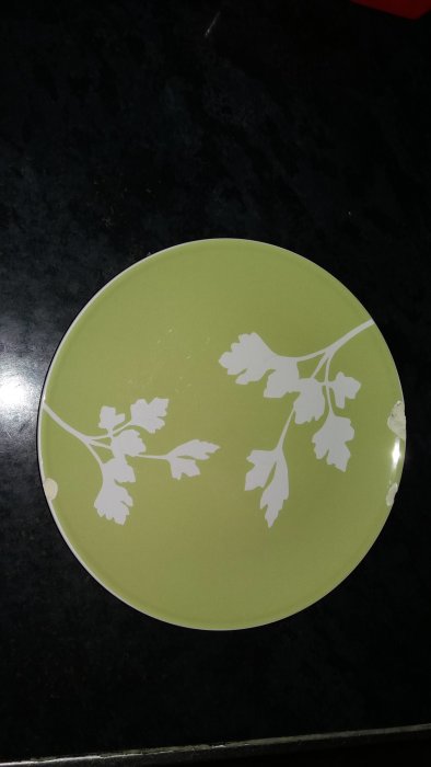 IKEA-porslinstallrik i olivgrön med vit bladmönsterdesign på en mörk bänkskiva.