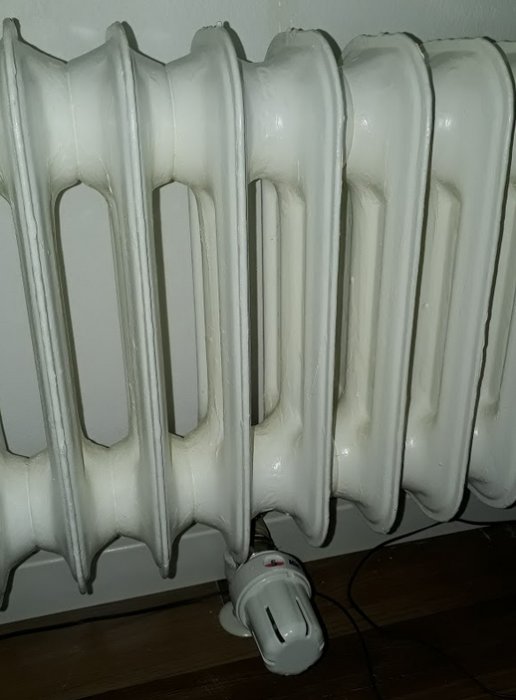 Vit ettrörsradiator med termostat nära golvet mot en vägg.