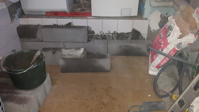 Byggarbetsplats med lecablock, murbruk, bygghink och kaklade väggar som förbereds för flytspackling.