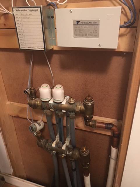 Värmesystemets fördelarenhet med ställdon och rörledningar på en trävägg, används för att stänga av golvvärme i en del av huset.