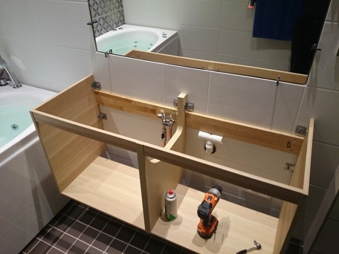 Pågående renovering av badrum med en delvis demonterad träinredning framför kakelvägg och ett badkar i bakgrunden.