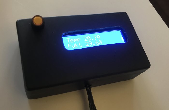 En fuktmätare i en svart låda visar temperatur och fuktighet på en digital skärm.