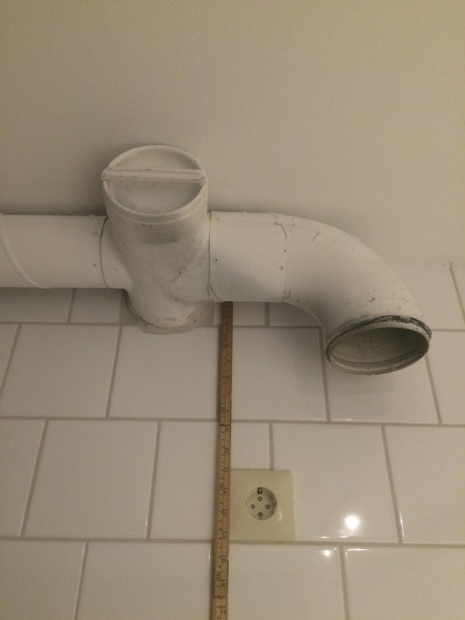 Ventilationsrör i kök med mätsticka och eluttag på kakelvägg
