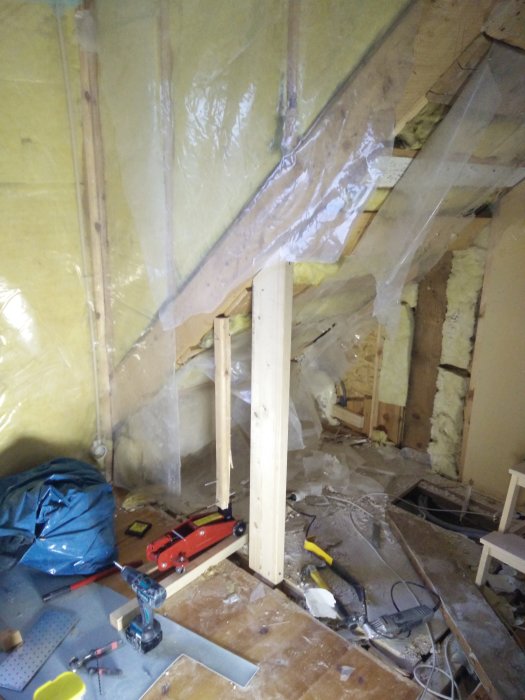 Nyinstallerat stödben i trä, stagat med en domkraft, under en snedtakskonstruktion på en byggarbetsplats.
