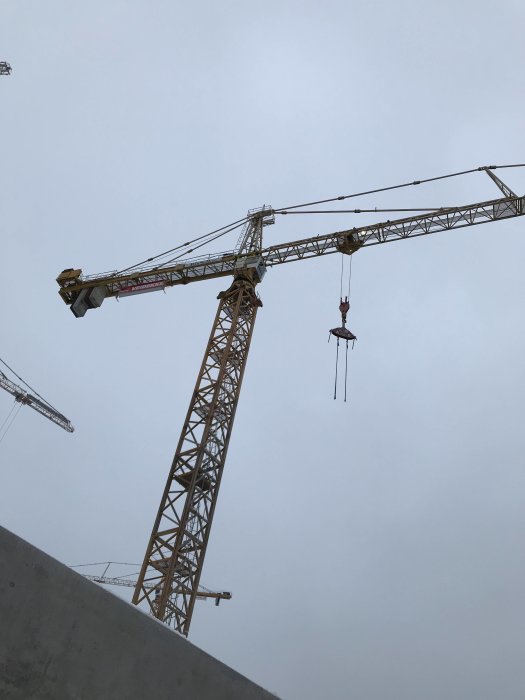 Två tornkranar mot en grå himmel, används vid montage av byggelement på en byggarbetsplats.