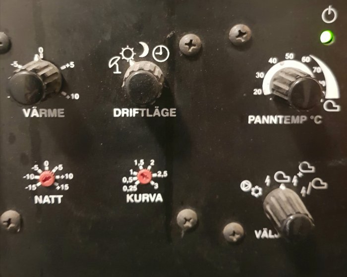 Värmesystemets kontrollpanel med inställningsrattar för värme, kurva och panntemperatur.