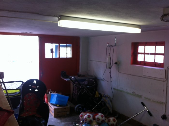 Garage interiör med oordning, barnstol, barnvagn och diverse föremål utspridda på golvet innan renovering.