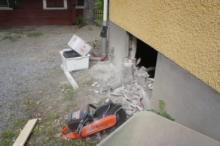 Hål i vägg för nytt fönster med murbruk och tegelstenar på marken; kapmaskin i förgrunden.