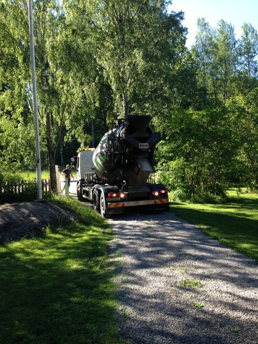 Betongbil från BetongKungen som levererar betong på en solig grusväg omgiven av gröna träd.