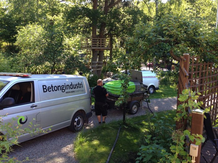 Betongbil och en skåpbil från Betongindustri parkerade utanför ett hus, en arbetare förbereder gjutning av betong.