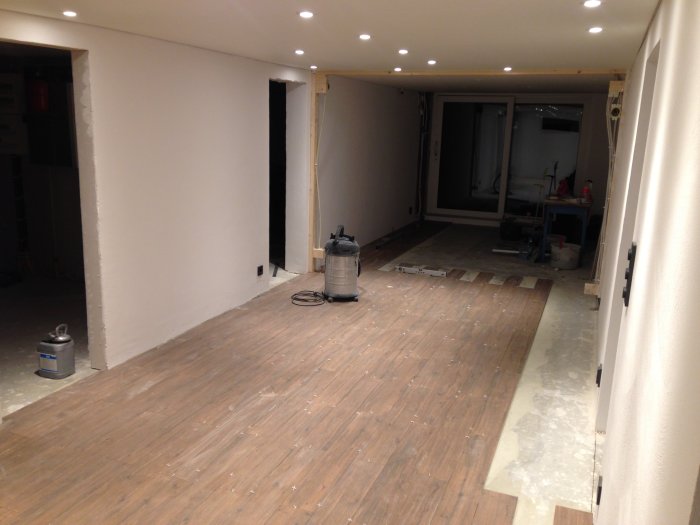 Renoverat rum med nyinstallerad träimitationsklinker på golvet och vitmålade väggar, under arbete.