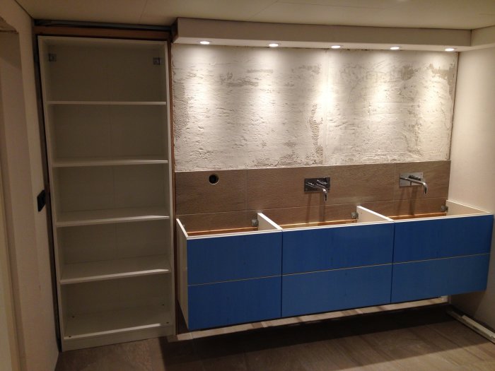 Nyrenoverat badrum med panelvägg, två handfat och blå skåp, bastupanelen ej färdigställd.