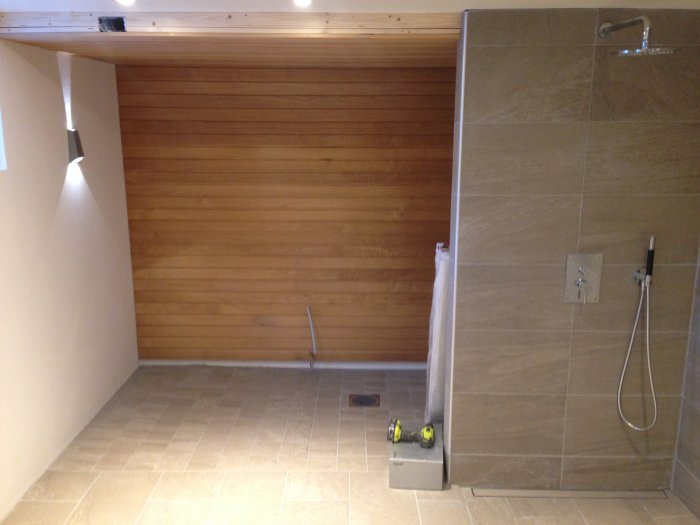 Halvfärdig bastu med träpanel bredvid en färdigställd dusch i badrum.