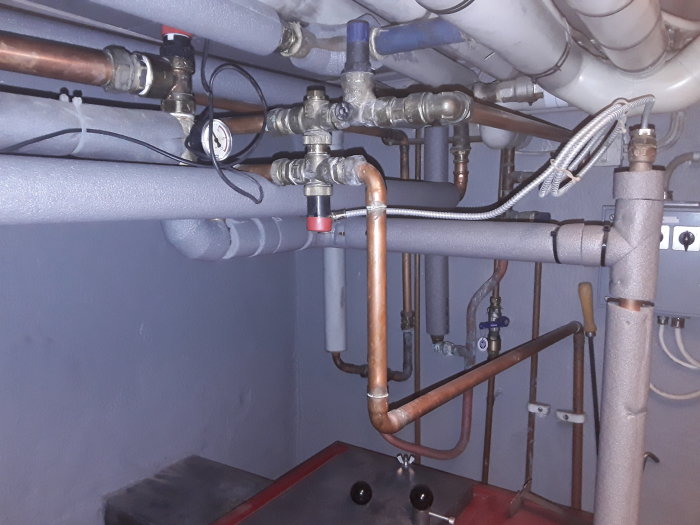Ett pannsystem med isolerade rör, märkningar och olika komponenter som shunt och cirkulationspump i ett förrådsutrymme.