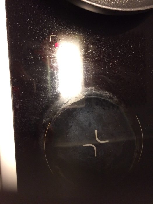 Kalk- och vattenfläckar på en svart spishäll med suddiga reflektioner av ljus.