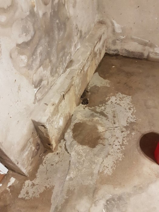Våt hörna i källare med synliga vattenskador och borrat hål i betongsulan som del av en temporär dräneringslösning.