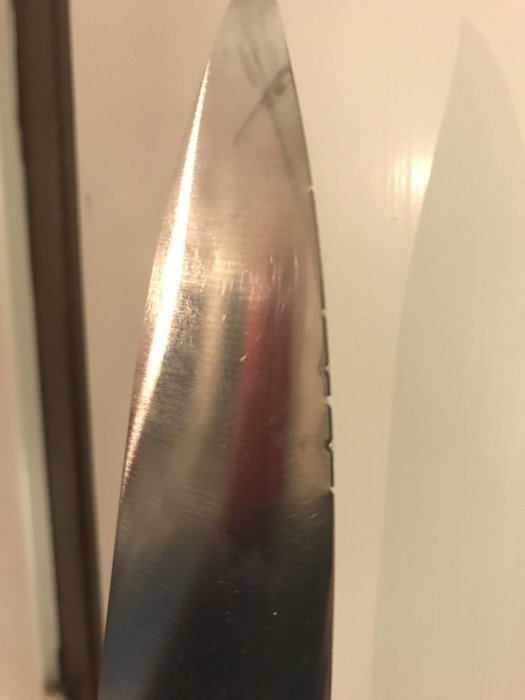 Närbild av en nyslipad knivs egg som reflekterar omgivningen, resultat av frihandslipning.
