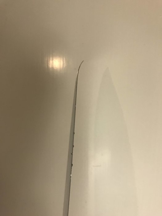 Slipad knivklinga med en spetsig topp och märken längs kanterna mot en ljus bakgrund.