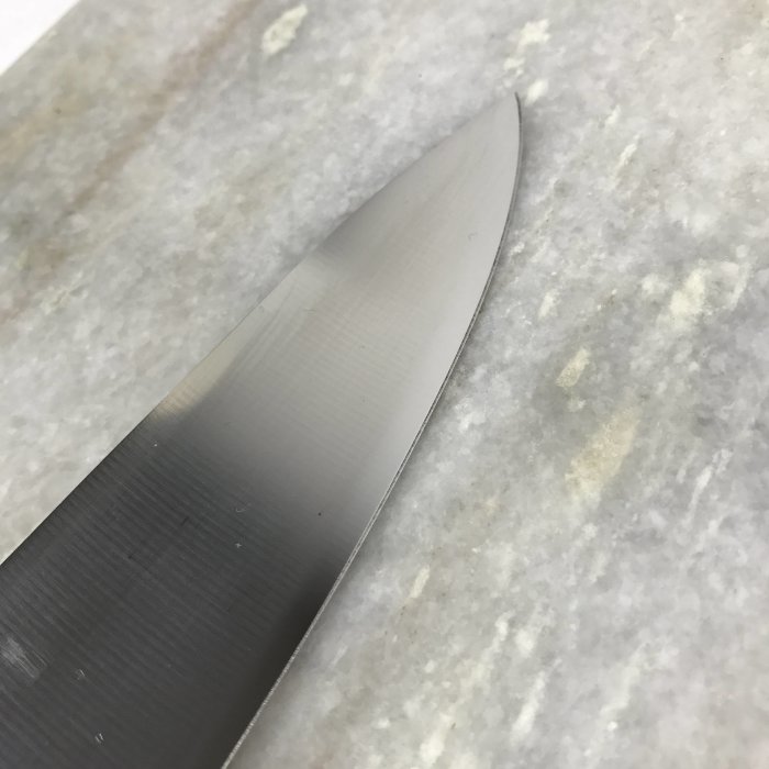 Nyligen slipad knivklinga på marmorbänk, skarpt och reflekterande blad, frihandslipning.