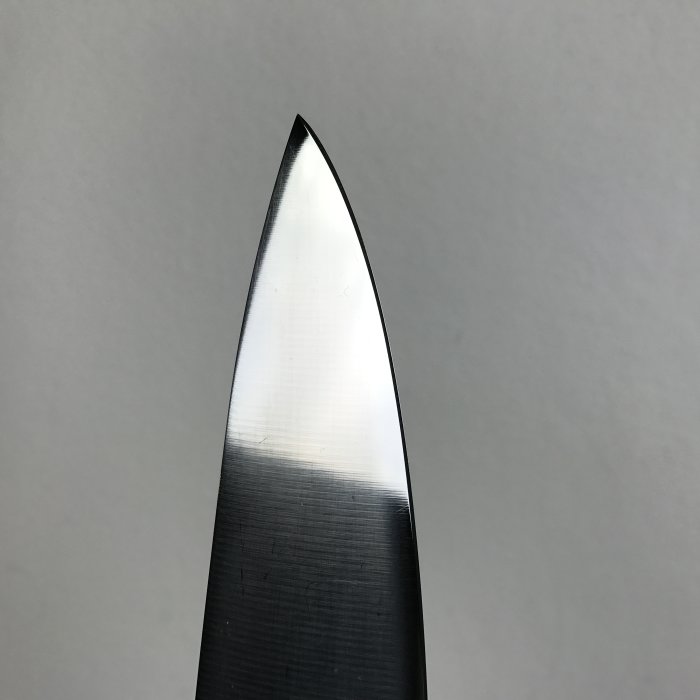 Nyslipad knivspets mot en ljus bakgrund som visar slipningens precision.